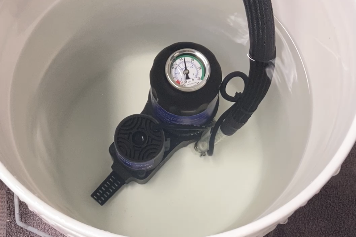 Black pressure gauge inside a white bucket on a dark surface